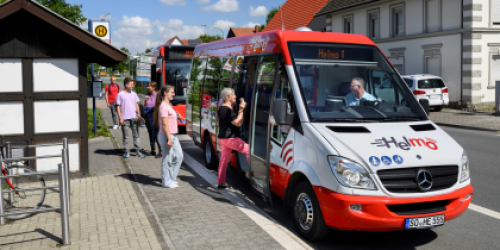 Rot-weißer Kleinbus Helmo steht an der Haltestelle. Drei Personen steigen ein. Rot-weißer Kleinbus Helmo steht an der Haltestelle. Drei Personen steigen ein.