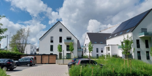 Drei weiße, neue Häuser eines Wohnquartiers mit Parkplätzen und Fahrradabstellanlage davor Drei weiße, neue Häuser eines Wohnquartiers mit Parkplätzen und Fahrradabstellanlage davor