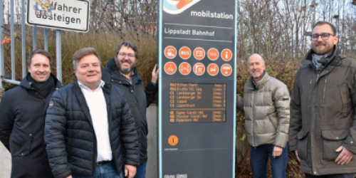 Fünf Männer stehen rechts und links einer ca 2 Meter großen Stele. Diese ist in dunklen Farben und zeigt auf einem Display Abfahrtszeiten an. Fünf Männer stehen rechts und links einer ca 2 Meter großen Stele. Diese ist in dunklen Farben und zeigt auf einem Display Abfahrtszeiten an.